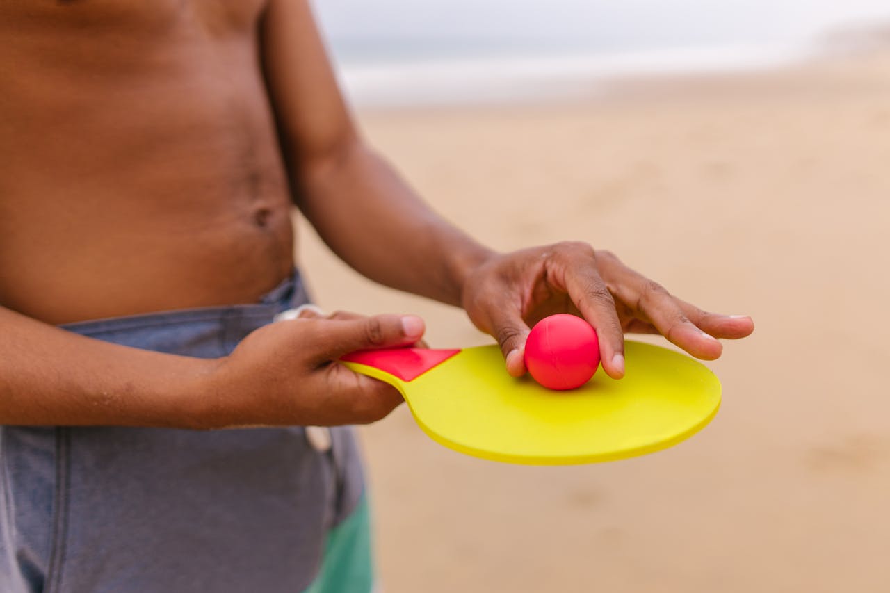 Close-up of hands holding a table tennis racket and ball on a beach day.
